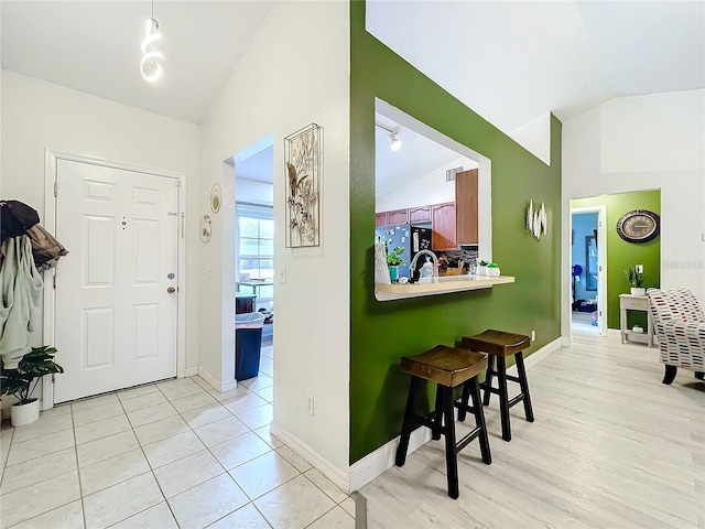 entryway with light tile patterned floors, visible vents, baseboards, and vaulted ceiling