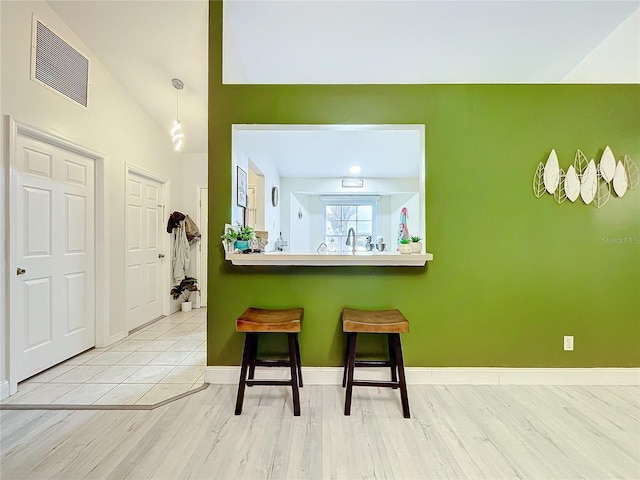 kitchen with baseboards, visible vents, lofted ceiling, a breakfast bar area, and light wood-style floors