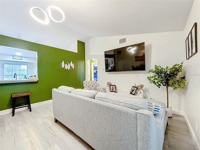 living area featuring vaulted ceiling, wood finished floors, visible vents, and baseboards