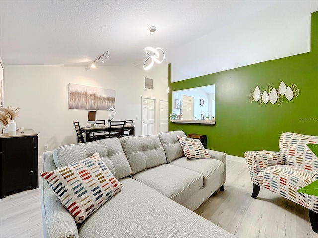 living area featuring lofted ceiling, visible vents, a textured ceiling, wood finished floors, and baseboards