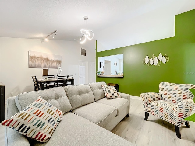 living area featuring lofted ceiling, visible vents, track lighting, wood finished floors, and baseboards