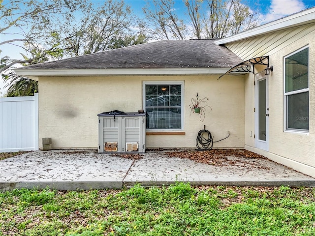 property entrance featuring a patio area, roof with shingles, fence, and stucco siding