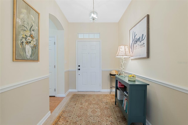 foyer featuring arched walkways, baseboards, and light tile patterned floors