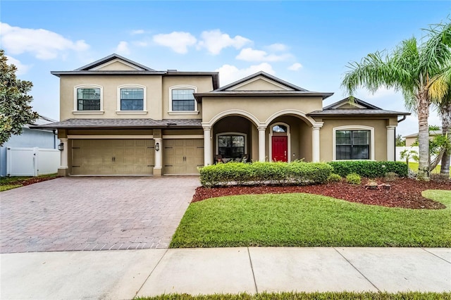 view of front facade with decorative driveway, stucco siding, a front yard, fence, and a garage