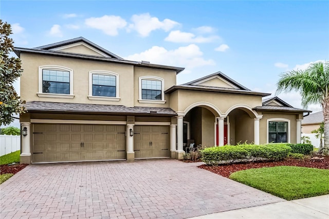 traditional-style house with decorative driveway, an attached garage, and stucco siding