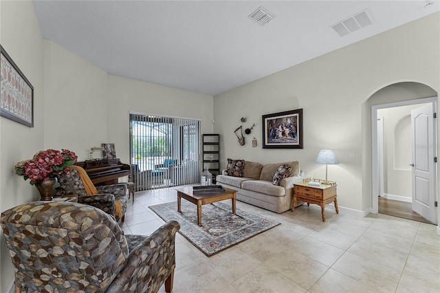 living room featuring arched walkways, light tile patterned floors, visible vents, and baseboards