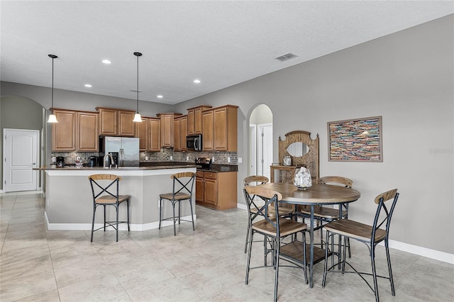 kitchen with arched walkways, decorative light fixtures, a center island with sink, dark countertops, and appliances with stainless steel finishes