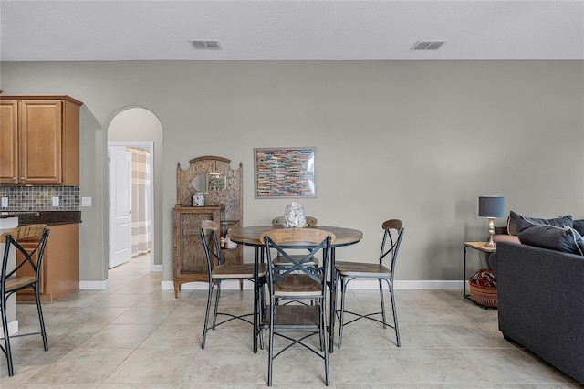 dining room featuring arched walkways, light tile patterned flooring, visible vents, and baseboards