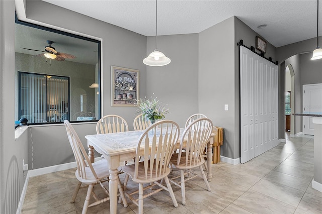 dining room with arched walkways, ceiling fan, baseboards, and a barn door