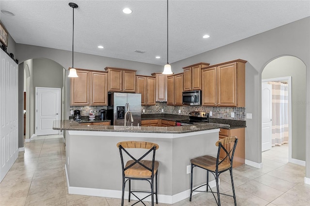 kitchen featuring arched walkways, stainless steel appliances, an island with sink, and pendant lighting