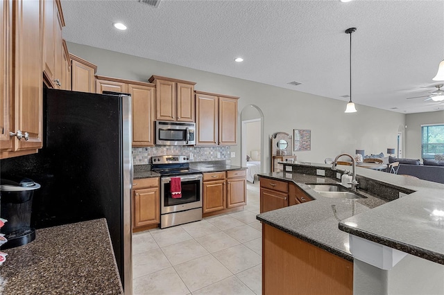 kitchen with a center island with sink, hanging light fixtures, appliances with stainless steel finishes, open floor plan, and a sink