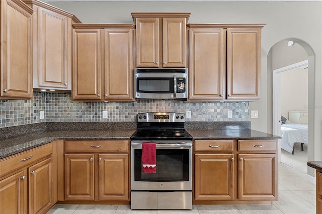 kitchen with appliances with stainless steel finishes, arched walkways, dark stone counters, and tasteful backsplash