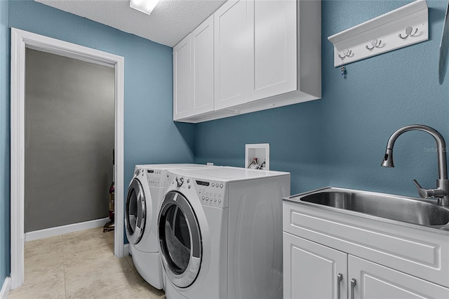 clothes washing area featuring a textured ceiling, a sink, baseboards, cabinet space, and washing machine and clothes dryer