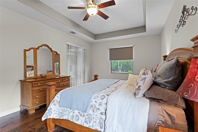 bedroom featuring a tray ceiling, visible vents, dark wood-type flooring, ceiling fan, and baseboards