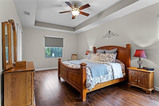 bedroom featuring baseboards, visible vents, a raised ceiling, dark wood-style floors, and ceiling fan