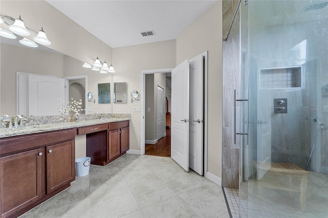 bathroom featuring double vanity, visible vents, a sink, a shower stall, and baseboards