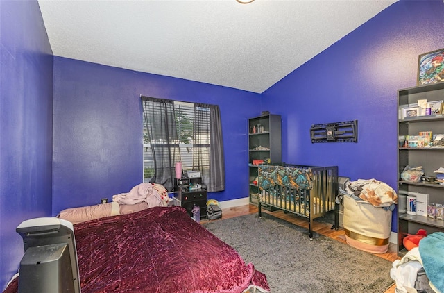 bedroom with lofted ceiling, a textured ceiling, baseboards, and wood finished floors