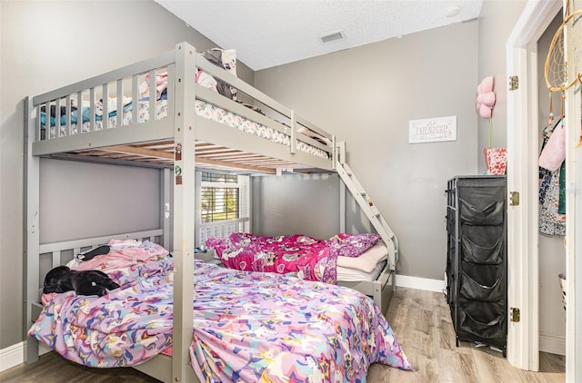 bedroom featuring a textured ceiling, wood finished floors, visible vents, and baseboards