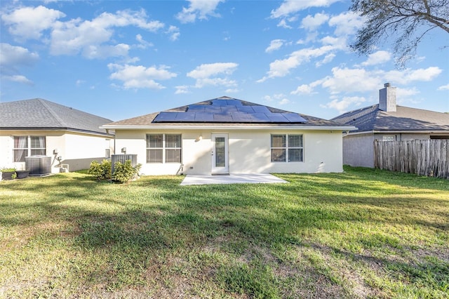 rear view of house featuring stucco siding, roof mounted solar panels, a lawn, and a patio