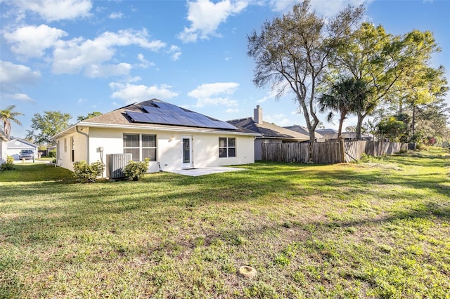 rear view of house with solar panels, a lawn, fence, and stucco siding