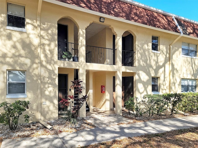 view of front of home with a balcony, mansard roof, and stucco siding