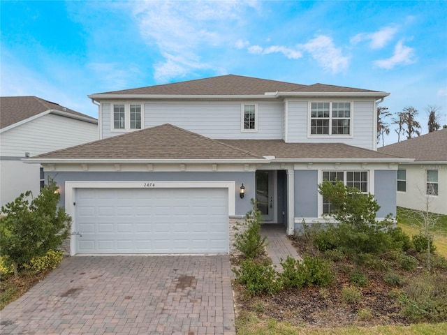 traditional-style home featuring decorative driveway, roof with shingles, and an attached garage