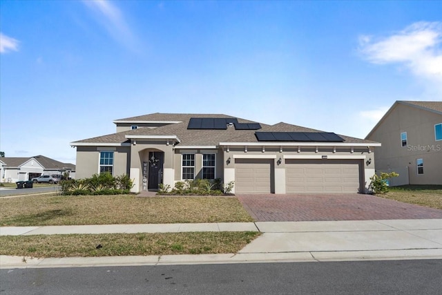 prairie-style house featuring an attached garage, solar panels, decorative driveway, stucco siding, and a front lawn