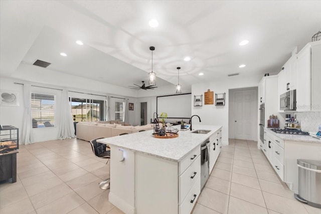 kitchen featuring white cabinets, open floor plan, hanging light fixtures, a kitchen island with sink, and a sink