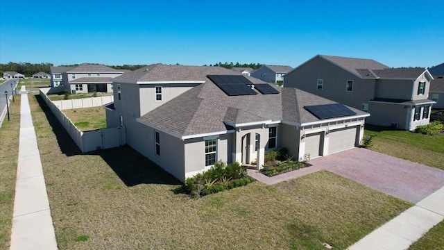 traditional-style home featuring decorative driveway, fence, a residential view, and roof mounted solar panels