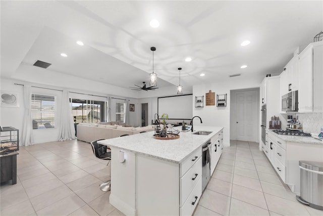 kitchen featuring decorative light fixtures, stainless steel appliances, open floor plan, a kitchen island with sink, and white cabinetry