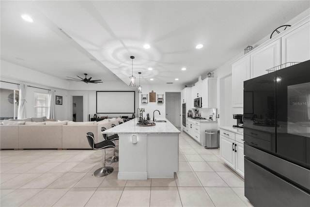 kitchen featuring a kitchen island with sink, a sink, stainless steel microwave, and white cabinetry