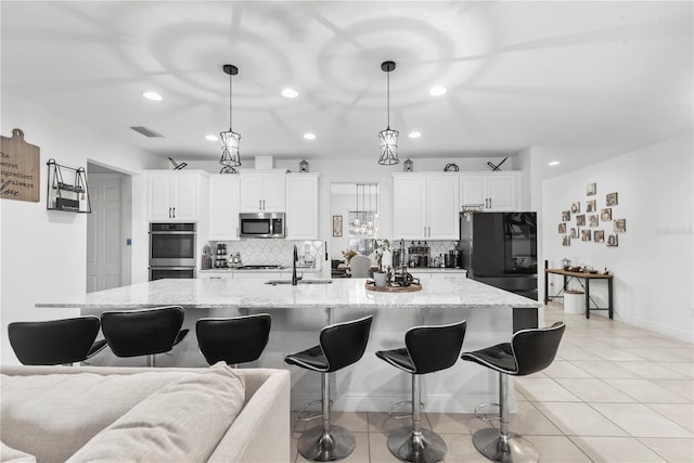 kitchen with stainless steel appliances, hanging light fixtures, white cabinetry, a sink, and a large island with sink