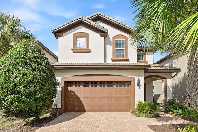 mediterranean / spanish house featuring an attached garage, a tile roof, decorative driveway, and stucco siding