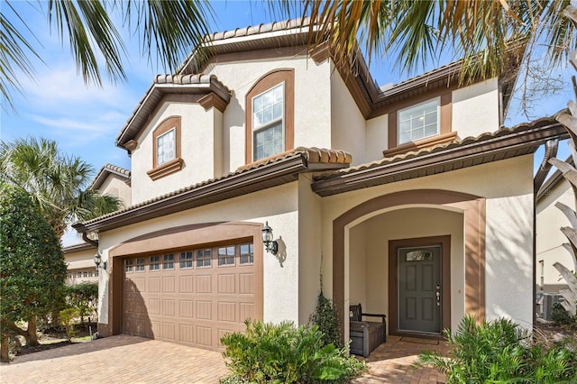 mediterranean / spanish-style house featuring decorative driveway, central air condition unit, an attached garage, and stucco siding