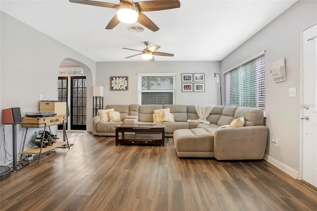 living room with dark wood-style floors, arched walkways, a healthy amount of sunlight, and visible vents