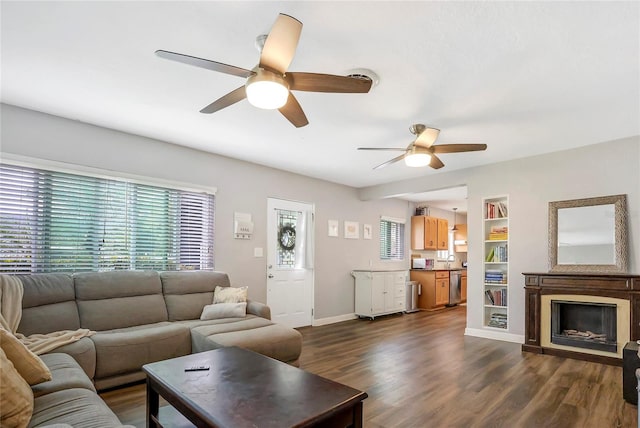 living room featuring baseboards, built in features, a ceiling fan, dark wood-style floors, and a fireplace