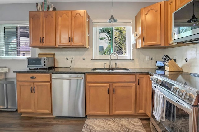 kitchen featuring dark wood-style floors, decorative light fixtures, tasteful backsplash, appliances with stainless steel finishes, and a sink