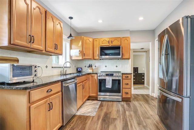 kitchen with pendant lighting, stainless steel appliances, light wood-style floors, a sink, and dark stone counters