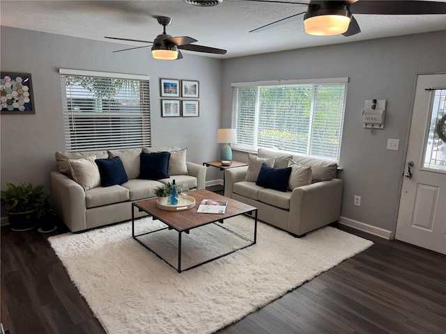 living area with a ceiling fan, dark wood-style floors, baseboards, and a textured ceiling