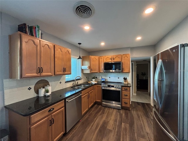 kitchen with appliances with stainless steel finishes, a sink, dark wood-type flooring, backsplash, and pendant lighting