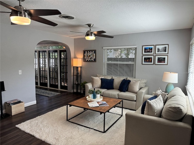 living area featuring a ceiling fan, arched walkways, wood finished floors, a textured ceiling, and baseboards