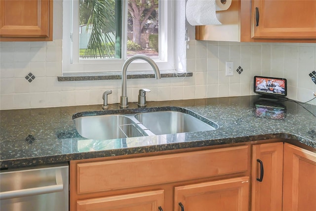 kitchen featuring a sink, stainless steel dishwasher, backsplash, and dark stone counters