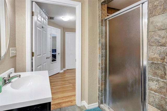 full bath featuring a stall shower, a textured wall, and vanity