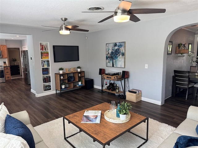 living area featuring a ceiling fan, arched walkways, wood finished floors, baseboards, and a textured ceiling