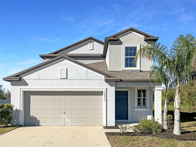 traditional-style house featuring an attached garage, roof with shingles, concrete driveway, and stucco siding