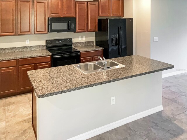 kitchen with baseboards, brown cabinetry, a kitchen island with sink, black appliances, and a sink