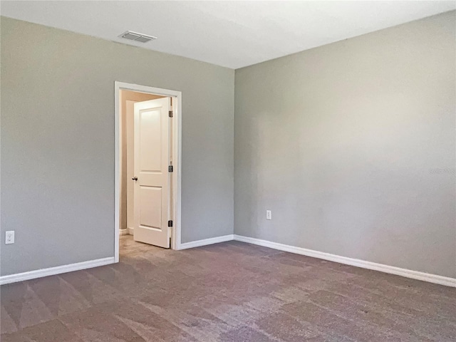 spare room featuring dark carpet, visible vents, and baseboards
