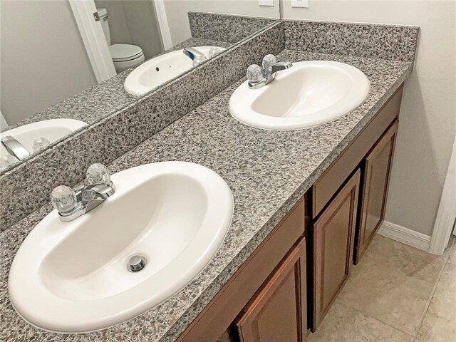 full bathroom with double vanity, a sink, and toilet