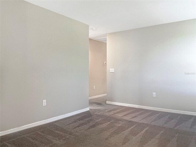 spare room with dark colored carpet and baseboards