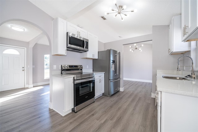 kitchen featuring arched walkways, appliances with stainless steel finishes, white cabinetry, a sink, and a chandelier